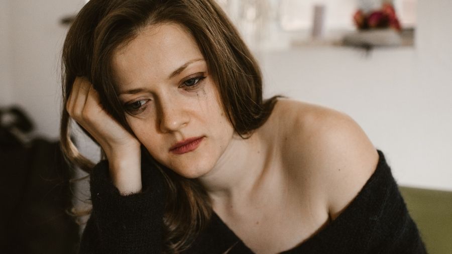 Woman with smudged mascara staring blankly, appearing hungover and heartbroken, conveying loneliness and emotional escape.