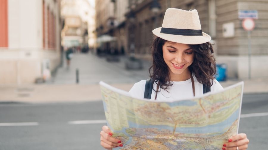 Smiling woman in a white t-shirt and hat holding a map on a busy city street