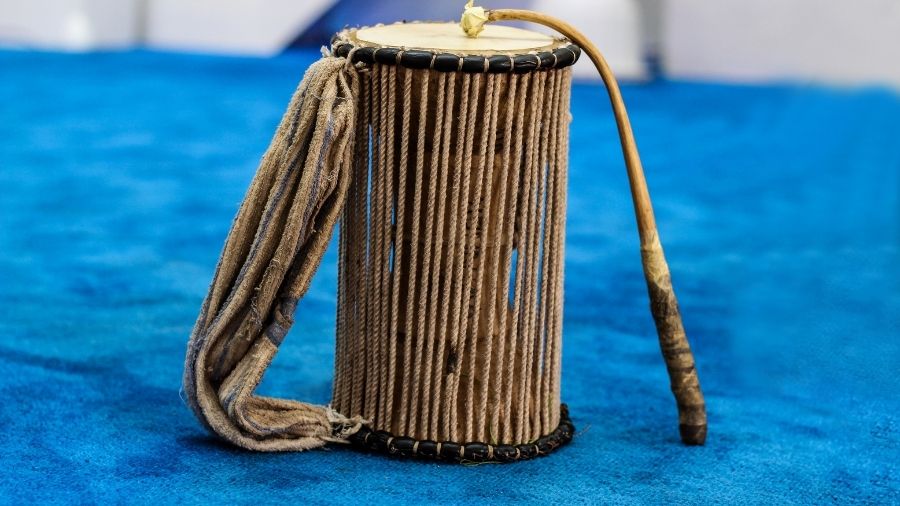 Talking drum with striker mallet isolated on a blue background.