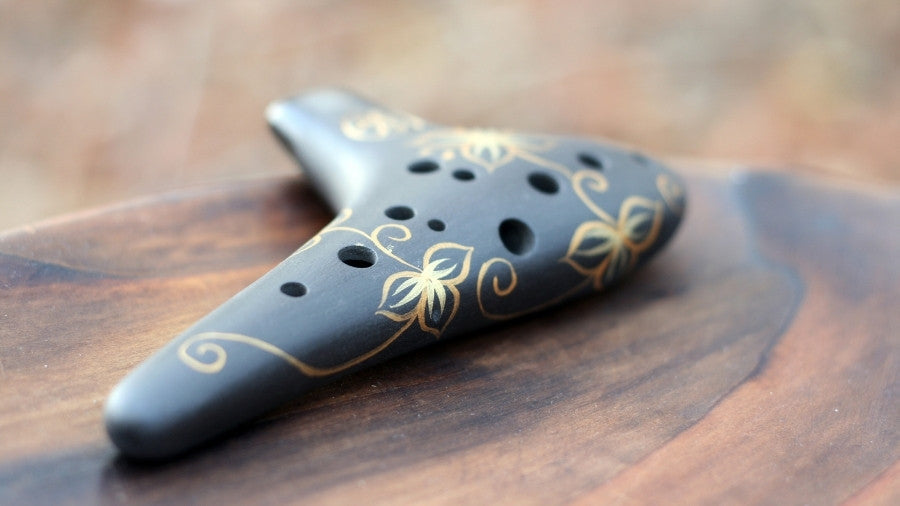Black Ocarina with Golden design on a wooden surface
