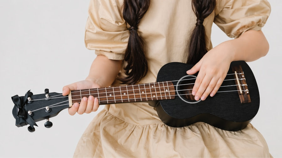 Girl holding a black ukulele on a light grey studio background