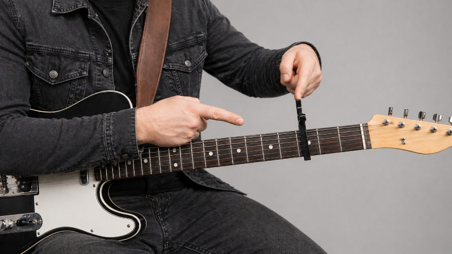 “Man with a guitar on his lap pointing at a guitar accessory.