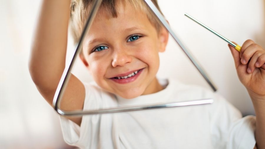 Small young boy holding a metal triangle and beater