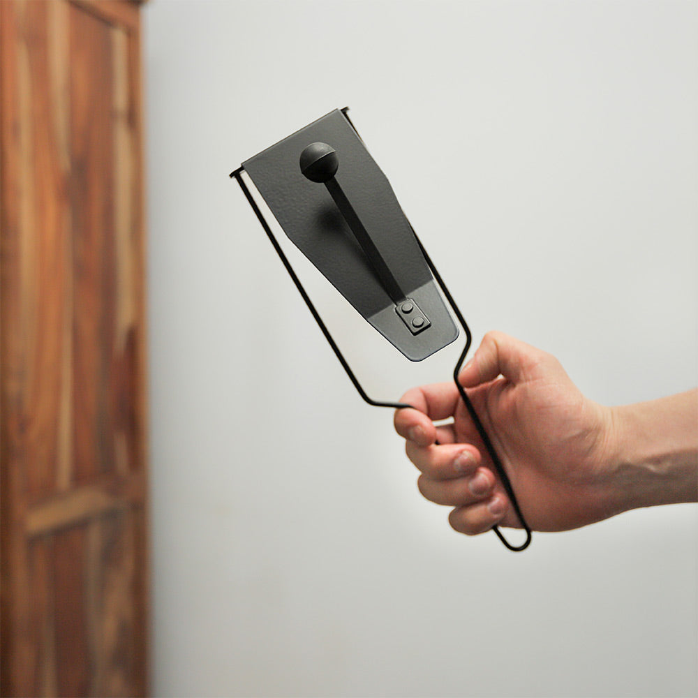 A simple black flexatone pitch-bending instrument held in hand, showing its compact size.