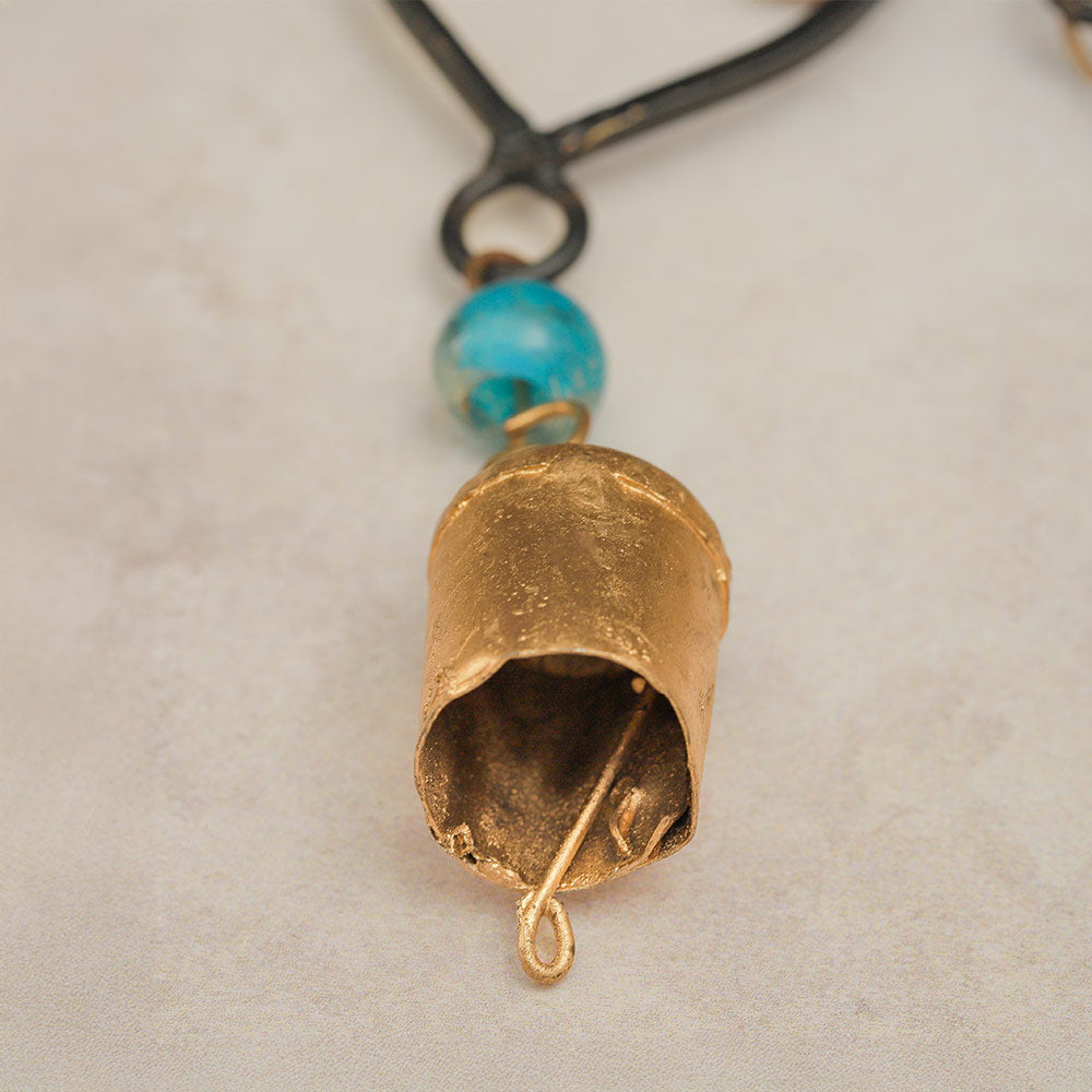 Close up of a single brass cowbell chime from the cast iron windchime, showing its texture and shape.