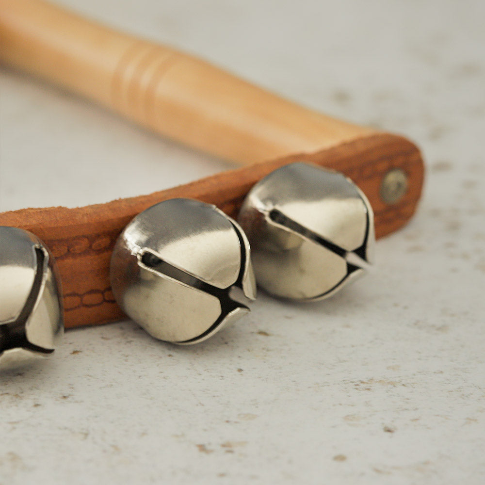 Close up of the sleigh bell shaker showing the wooden handle, leather strap and stainless steel bells