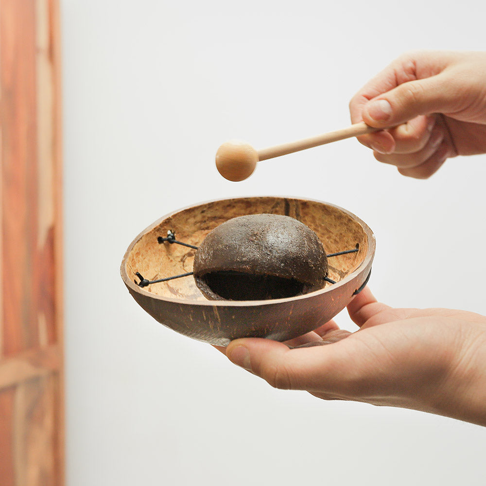 Coconut husk tone block percussion instrument with beater held in hand to show its size and scale.