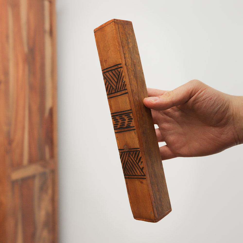 Jati block rainstick wooden shaker with tribal design, shown in hand for scale.