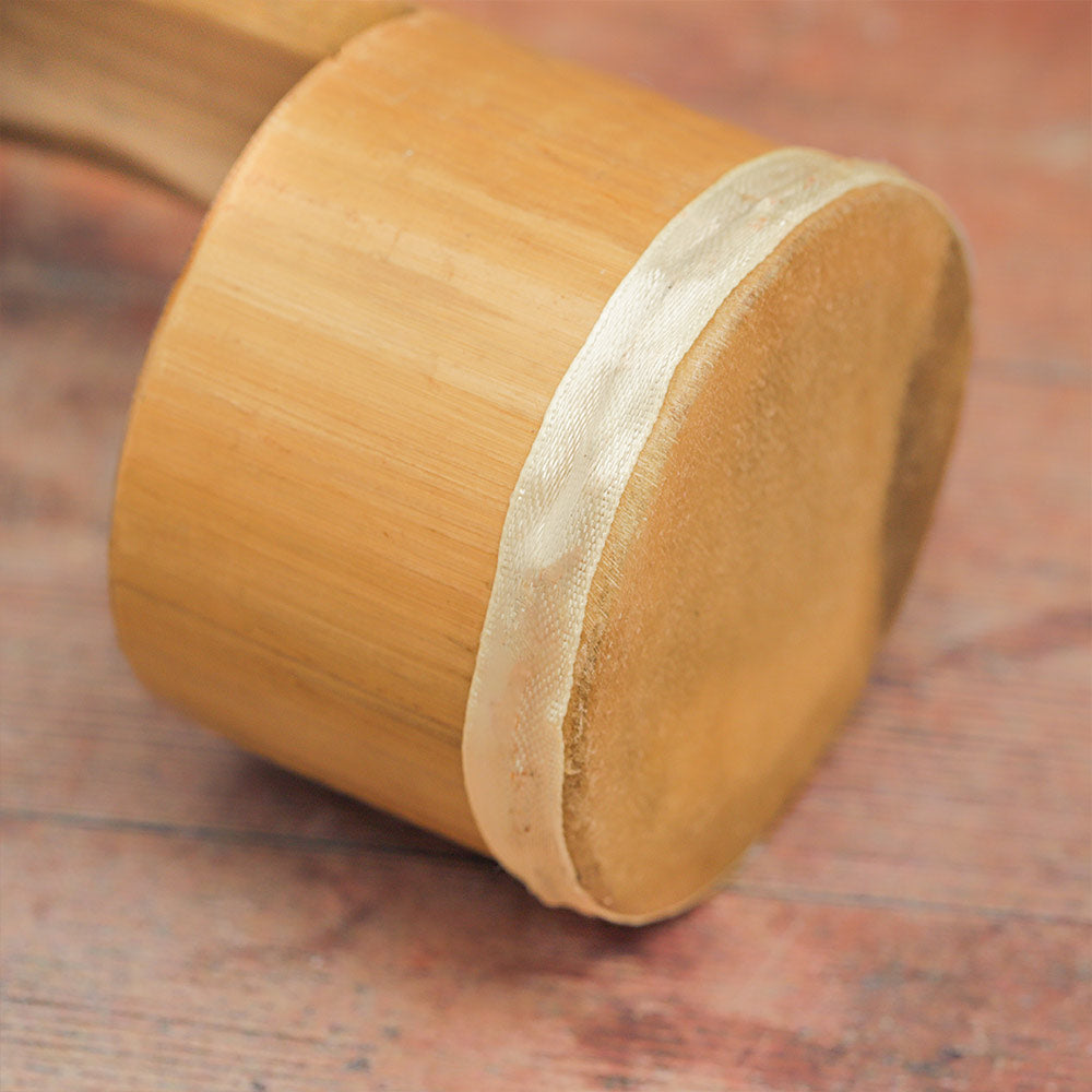 Close-up of the Jati Guiro Drum Shaker showing the textured bamboo, animal hide drum head, and white ribbon.
