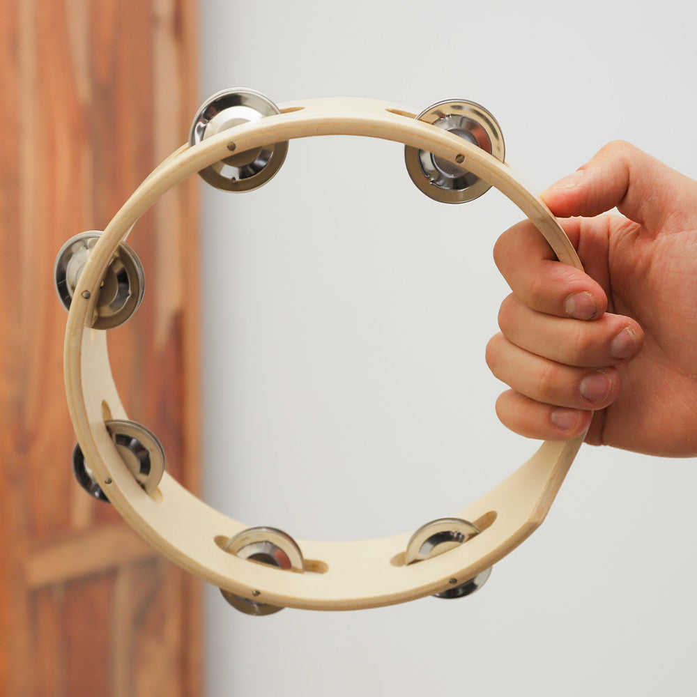 Close-up of a Rebana tambourine percussion instrument with a wooden frame and metal bells, held in the hand to show scale.