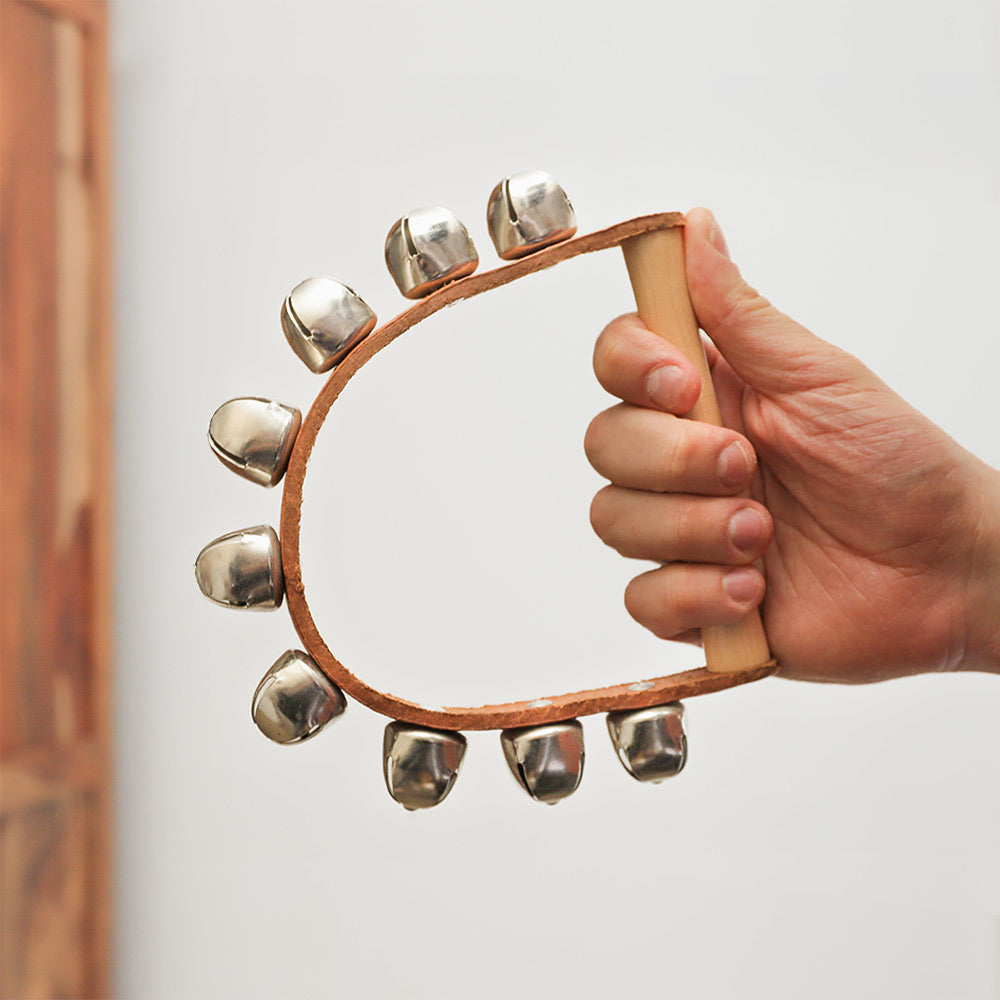 Sleigh bell shaker featuring 9 metal bells attached to a leather band with a solid wood handle, held in hand for scale.