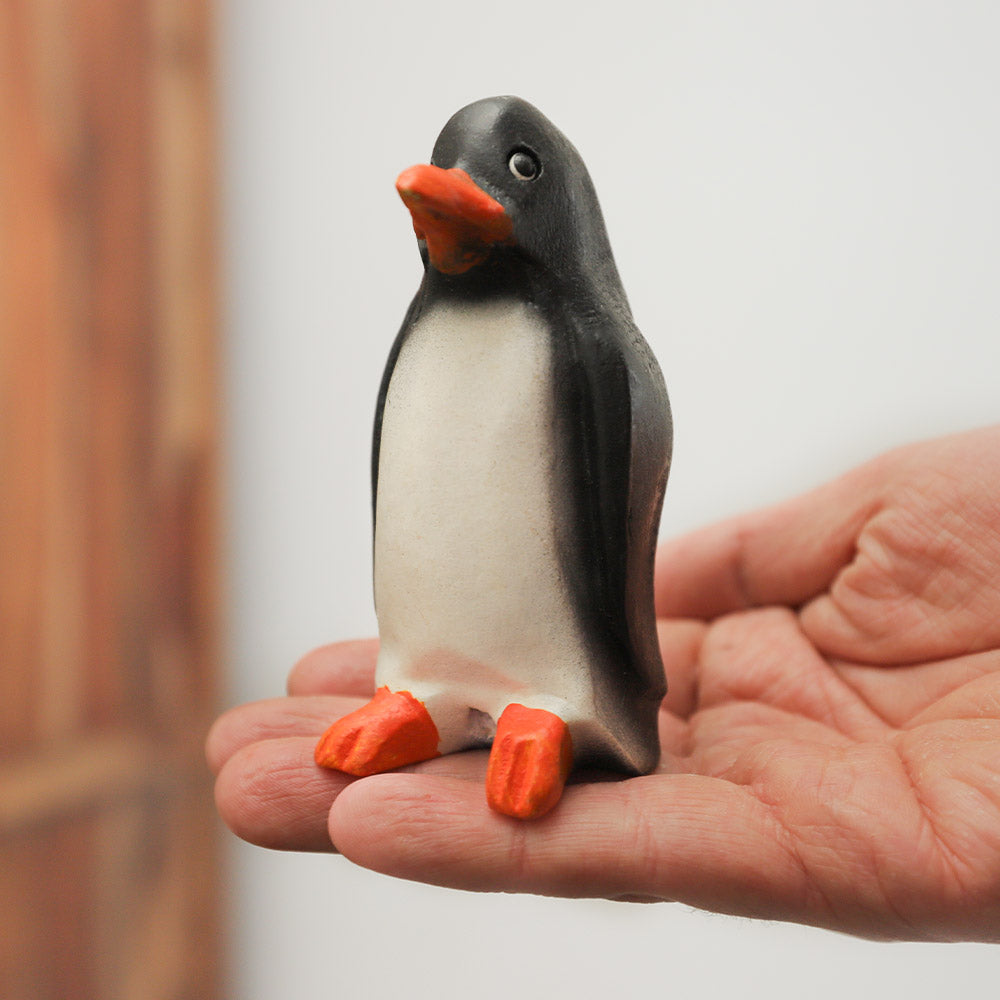 Solid wood penguin whistle ornament from Thailand, black and white with orange feet and beak.