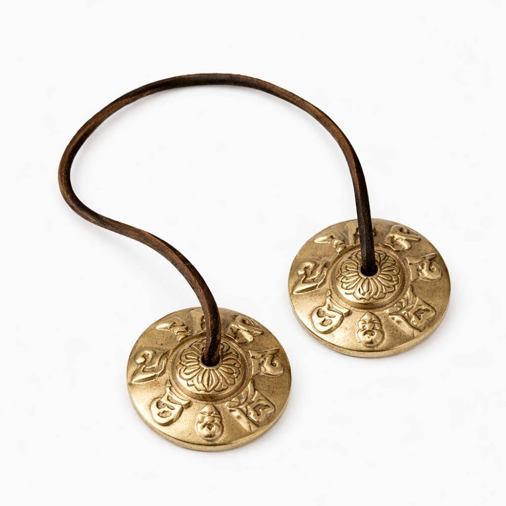 Pair of brass tingsha prayer bells attached to leather handle on a white studio background