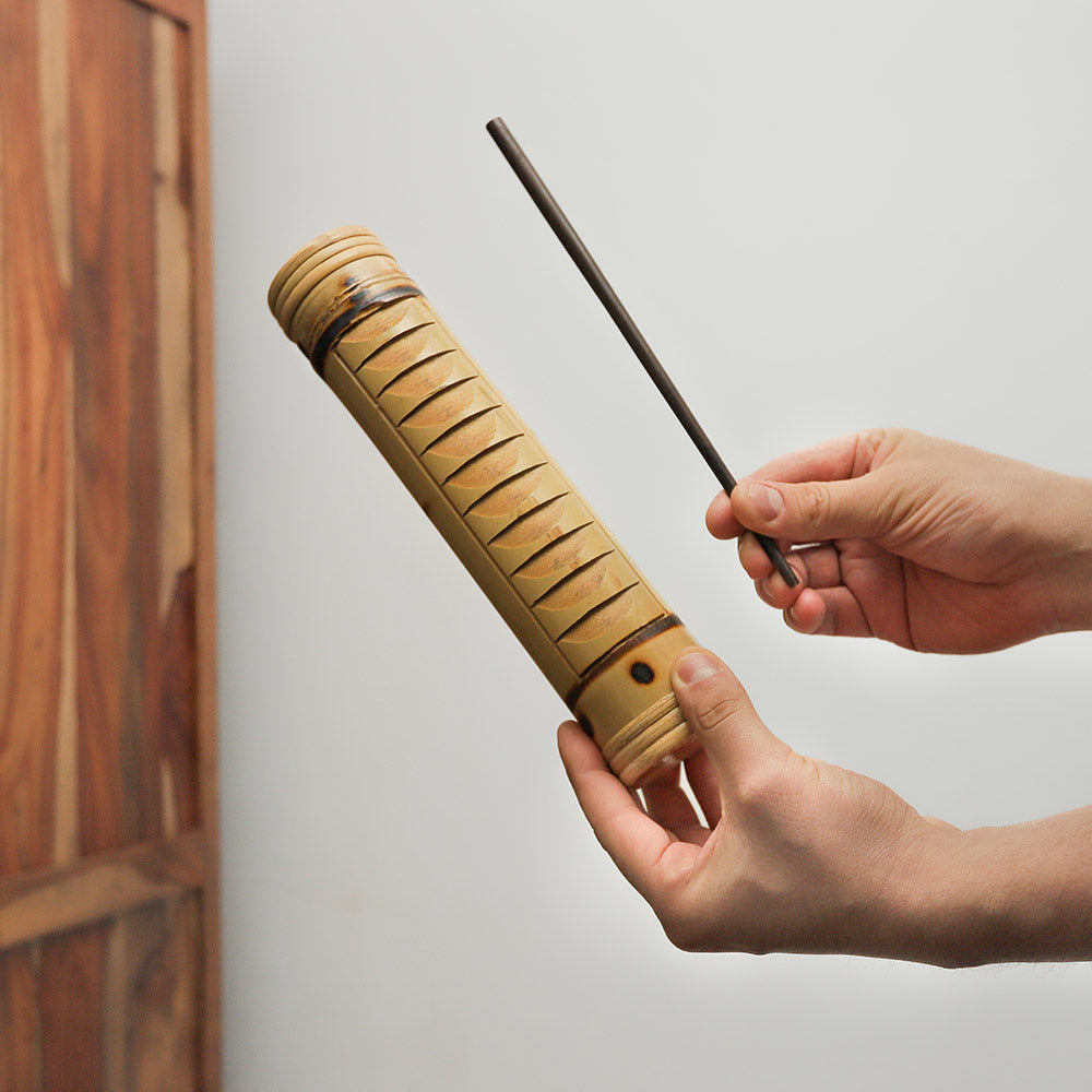 Toko guiro shaker held in hand with scraper, demonstrating its size and design.
