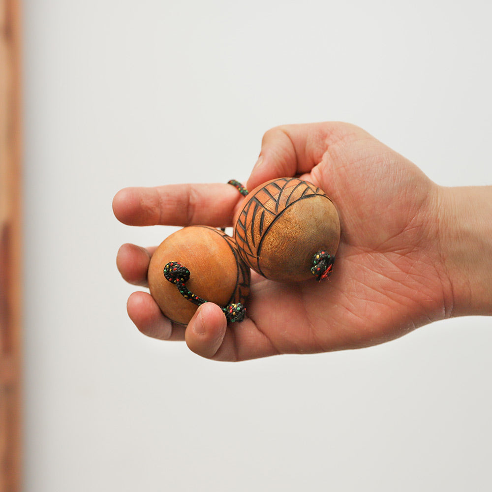Close-up of the wooden Kashaka shaker balls held in hand to show scale, featuring a geometric design.