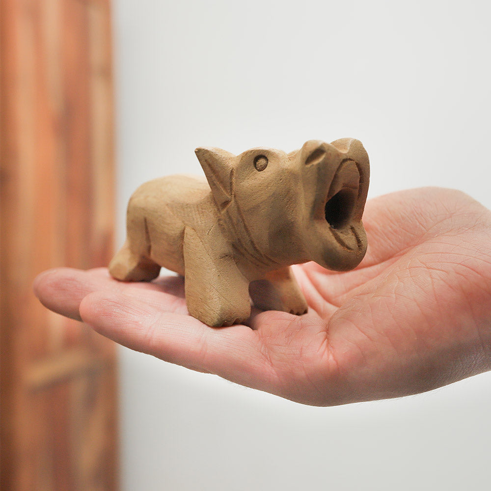 Wooden pig whistle held in hand, showing its size and carved design.