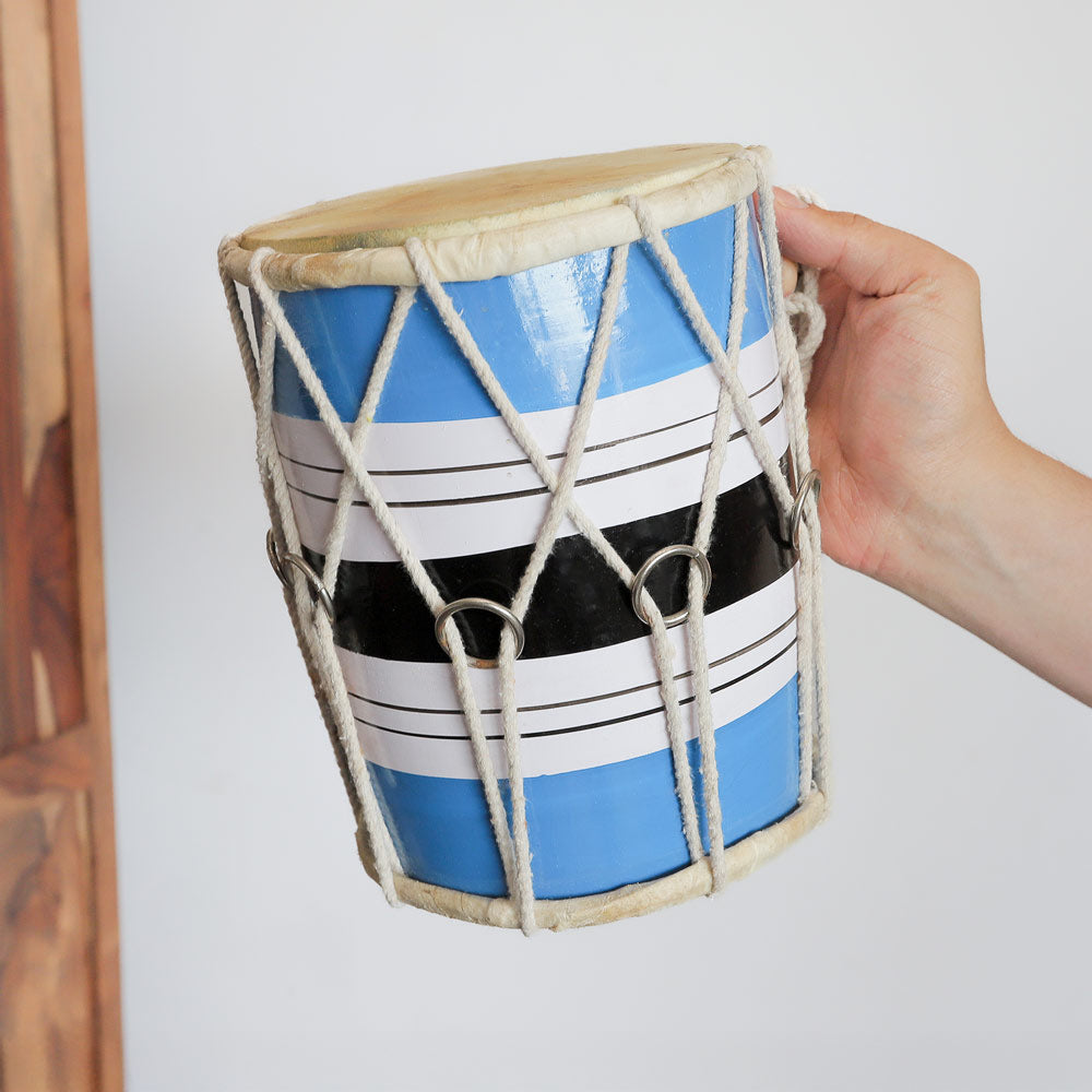 A traditional Indian dholak drum being held in the hand to show scale