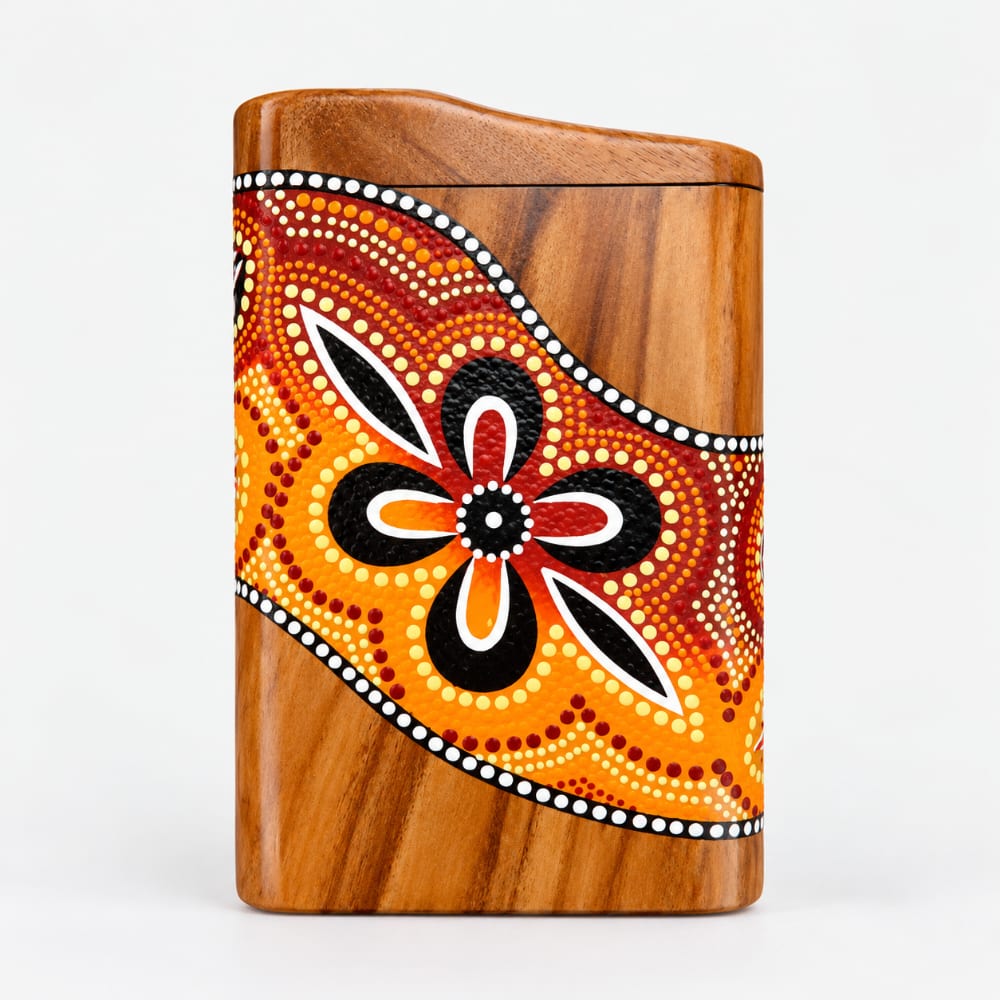 hand-painted Aboriginal dot art design on a pocket didgeridoo in orange, red, black, and white on a natural wood grain background, set against a studio background.
