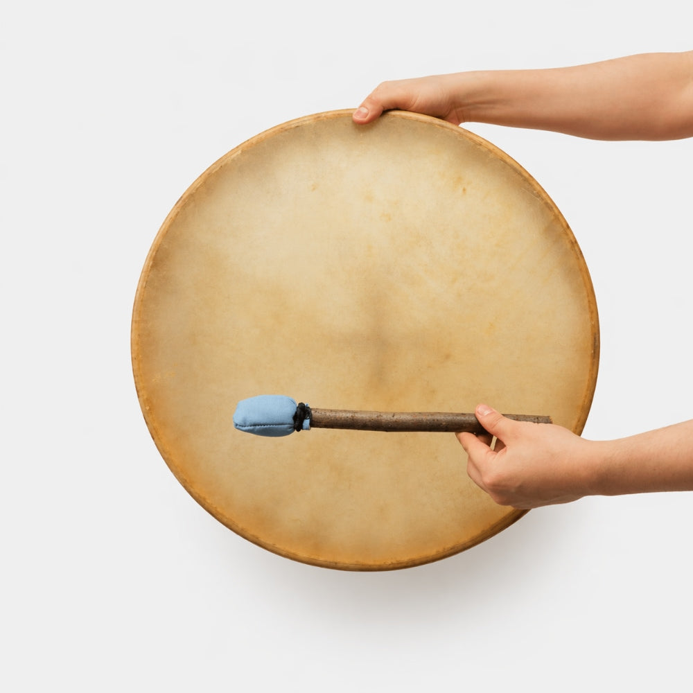 Person holding a 12 inch khenhi cow hide shamanic drum with a blue tipped mallet beater on a white studio background