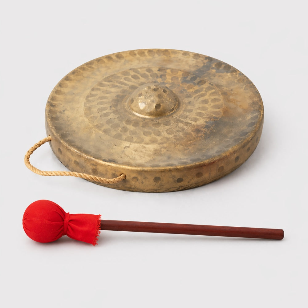 Traditional brass gong with hangining loop and red mallet beater on a light gray studio background