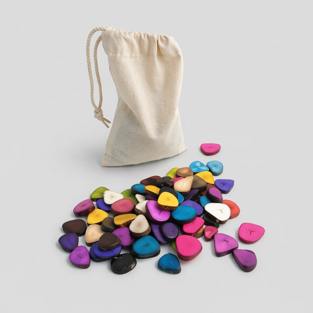 259 grams of colourful natural dyed tagua seeds for craft with a beige drawstring bag on a light gray studio background