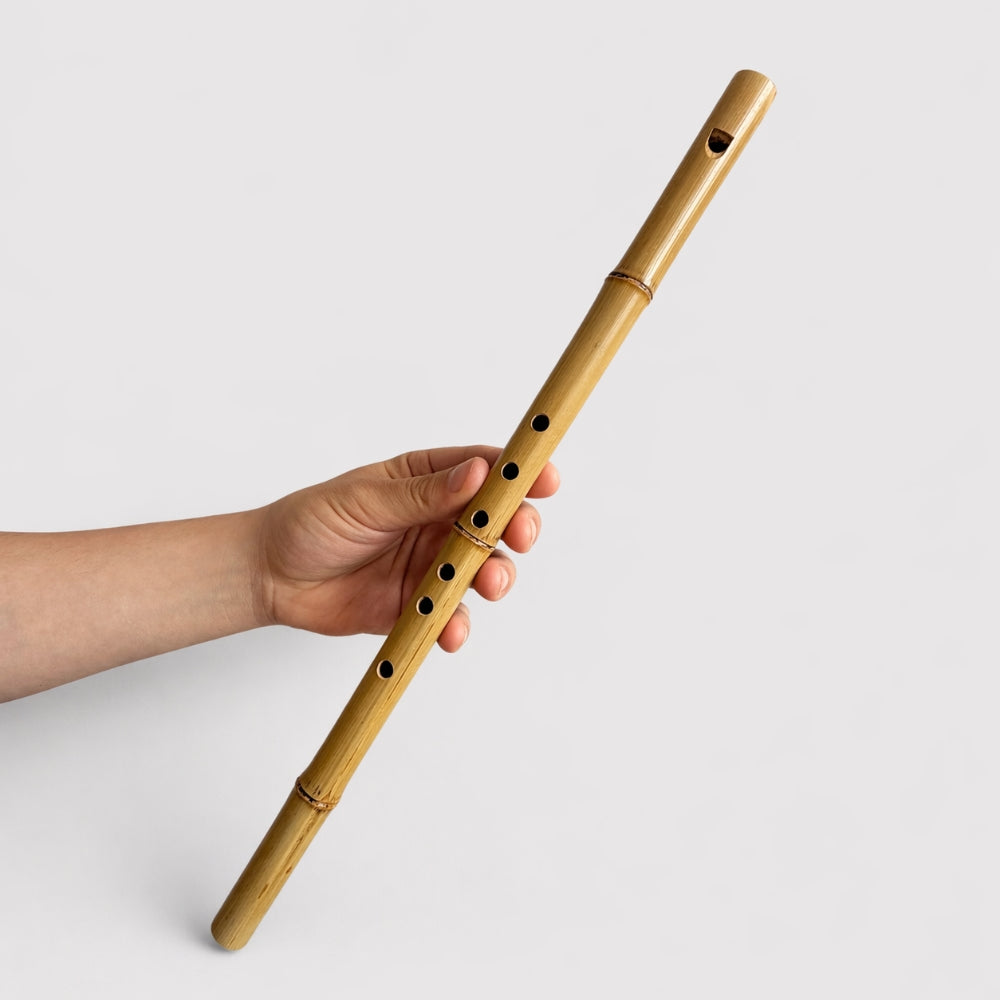 Hand holding a bamboo flute on a light gray background