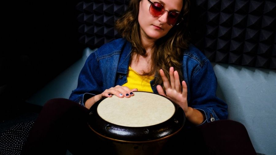 Young woman playing a djembe drum while sitting on the floor in a recording studio. Ethnic African percussion instrument.