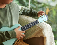 A boy in a green sweater tuning his ukulele.