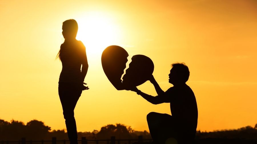Silhouette of a man holding a broken heart while a girl stands with her back turned to him.