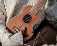 Close-up of a person holding a ukulele, showing their hands and part of the instrument.
