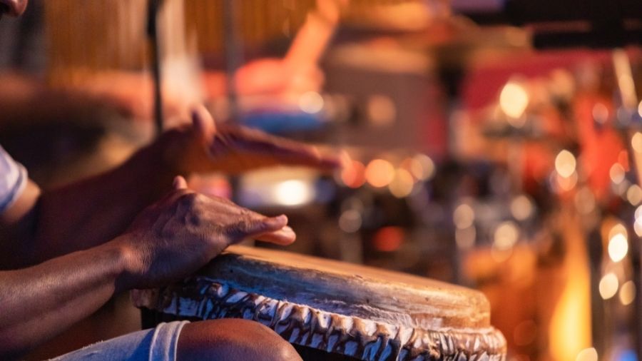 A close-up action shot of hands striking a Djembe near the rim, mid-slap, with motion blur or a subtle emphasis on finger position.