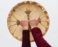 Cows hide shamanic drum with two hands holding the grip