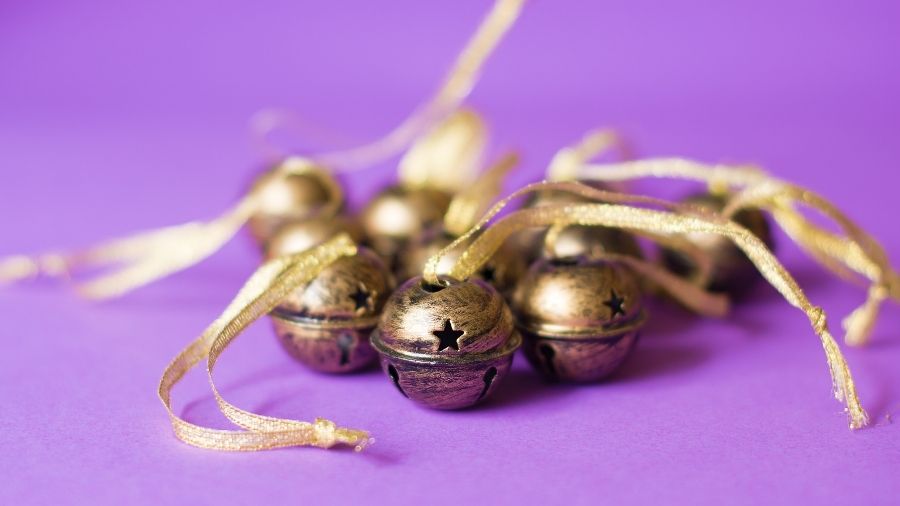 Brass-coloured metal sleigh bells with star cutouts and golden ribbon on purple background.
