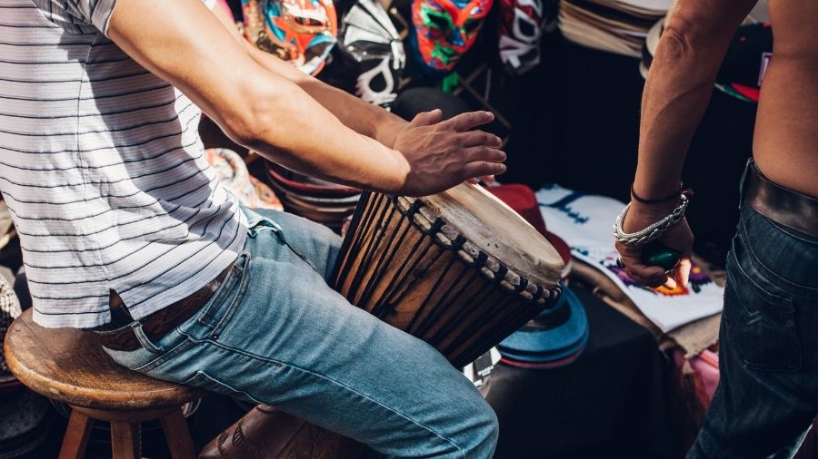 Man sitting on a chair playing a djembe drum.