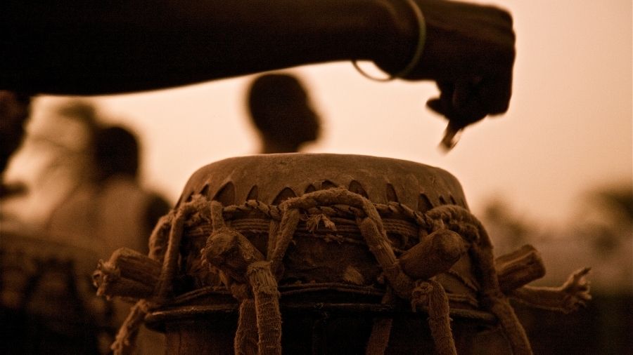 Silhouette of a person playing a Djembe drum and carefully tending to the instrument.