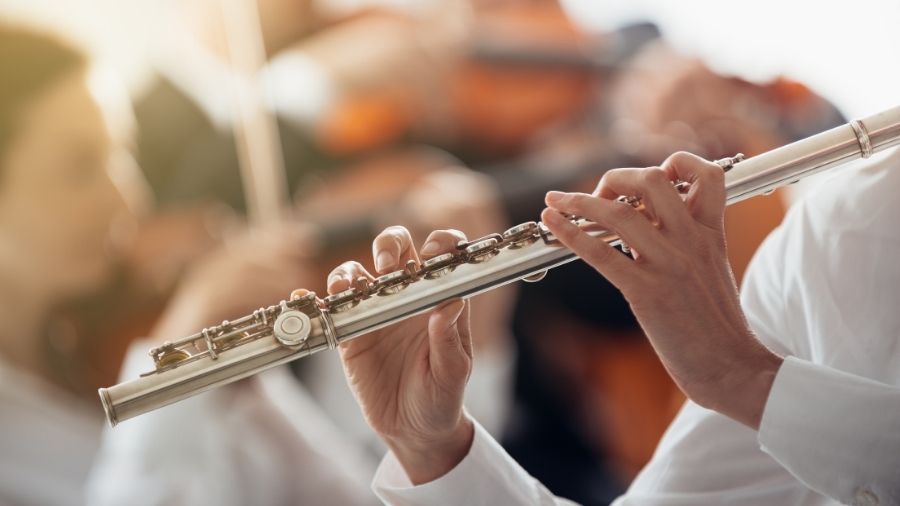 Professional flute player performing, wearing white, in focus with a blurred background.