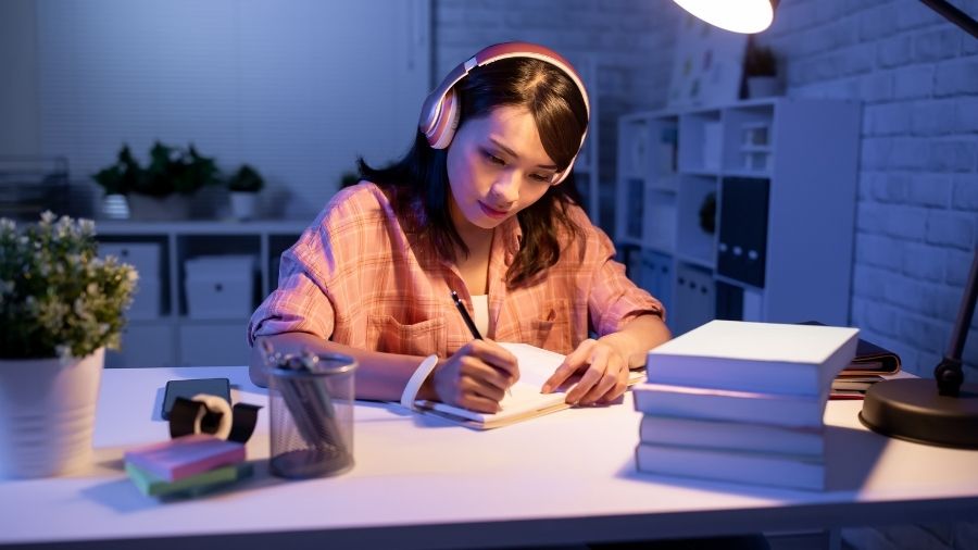 An Asian student studying intently, wearing a headset, surrounded by study materials.