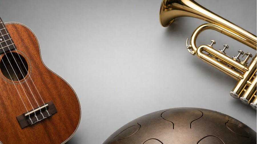 Cropped ukulele, trumpet and handpan on a clean silver grey background symbolising overpriced musical instruments