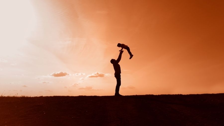 Silhouette of a father tossing his child into the air against a red sunburst sky, symbolizing love, joy, and protection.