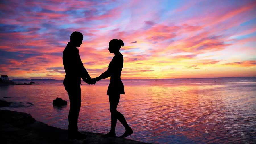 couple on beach with sunset holding hands