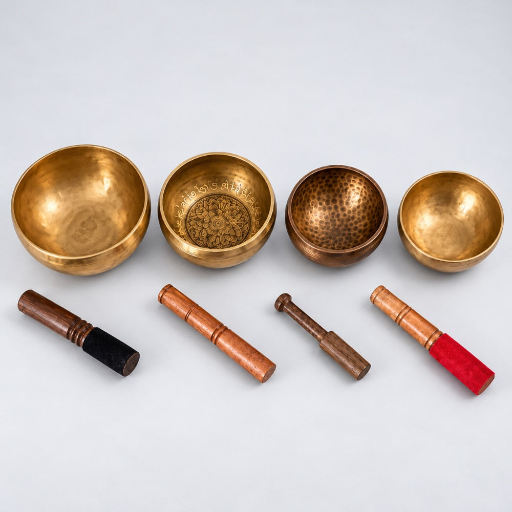 Four brass singing bowls of different sizes arranged in a row, with four wooden mallets below them on a light gray background.