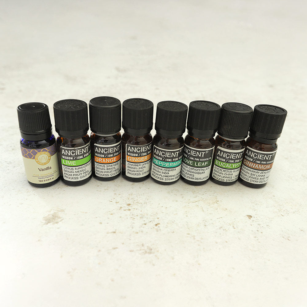 A collection of essential oils including Lime, Orange, ginger, vanilla, peppermint, clove leaf oil, eucalyptus and cinnamon oil displayed in glass bottles with labels.