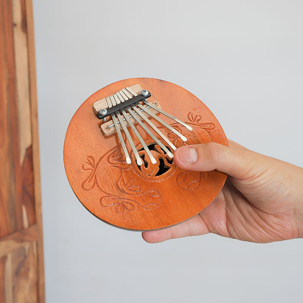 The natural coconut shell 7 note thumb piano kalimba with carved gecko design held in the hand to show scale size.