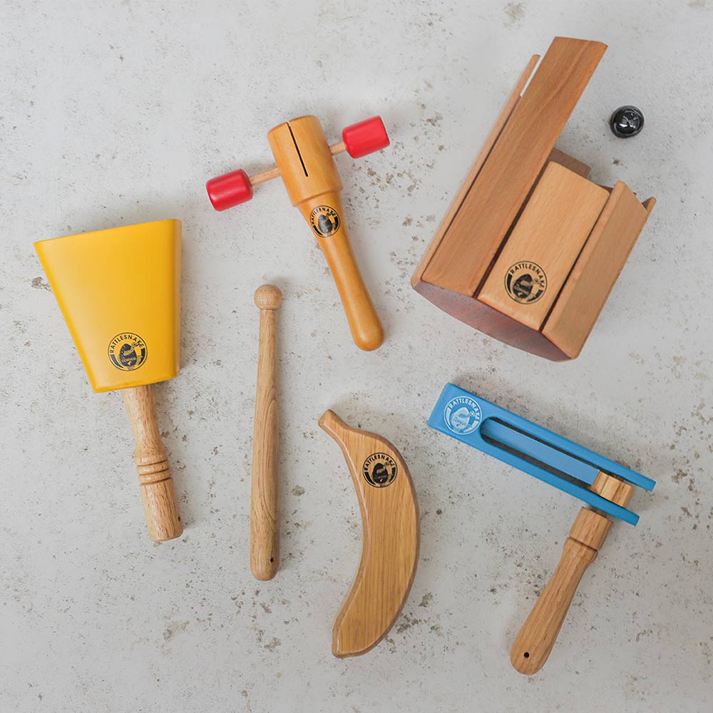 Bundle of rattlesnake percussion instruments including yellow cowbell with beater, t shaker, banana shaker, blue football ratchet  and xylophone laying down with marble