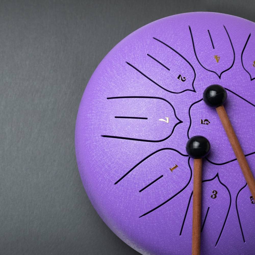 Purple tank drum with two mallets on a gray background