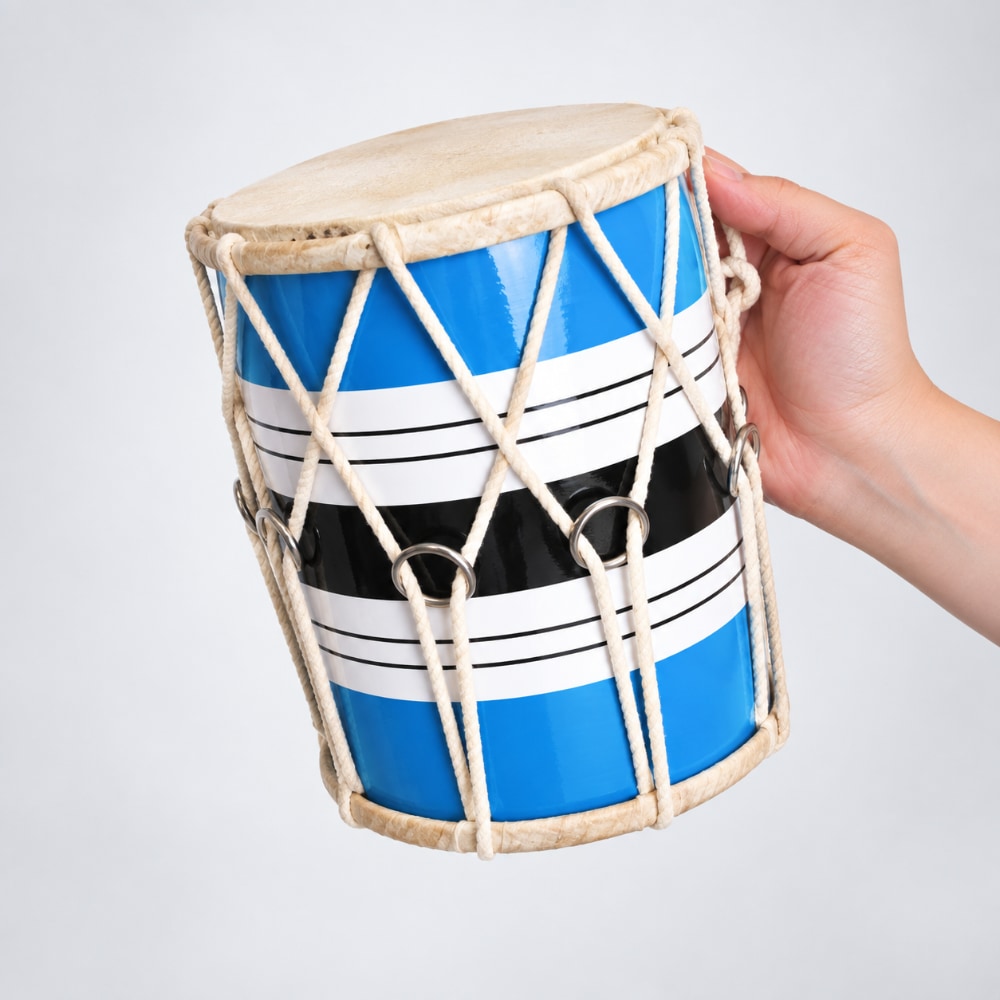 A hand holding a small dholak drum with a blue, white, and black striped body, beige rope lacing, and a natural drumhead, set against a plain light gray background.