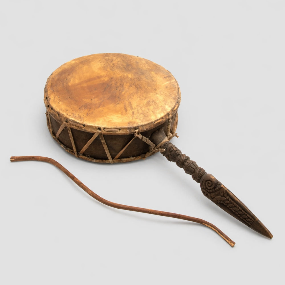 Traditional large Nepalese Dhyangro drum with hand carved detailed stake handle with a curved wooden beater stick on a light grey studio background
