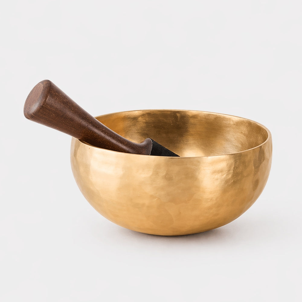 Brass bon singing bowl with wooden mallet and suede tip on a white studio background