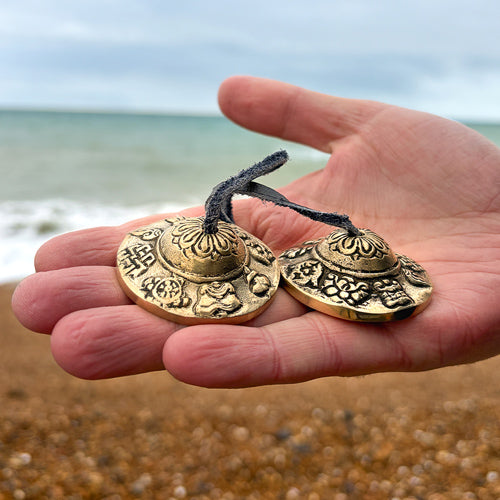 Hand holding two tingsha bells against a beach background