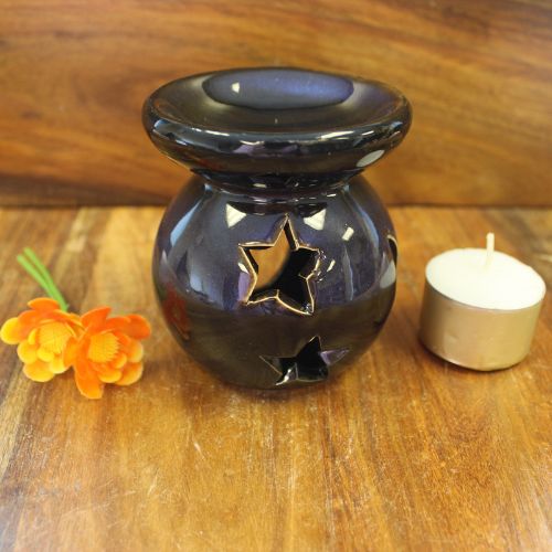 Black ceramic oil burner with star design on a wooden surface with a candle and flowers.